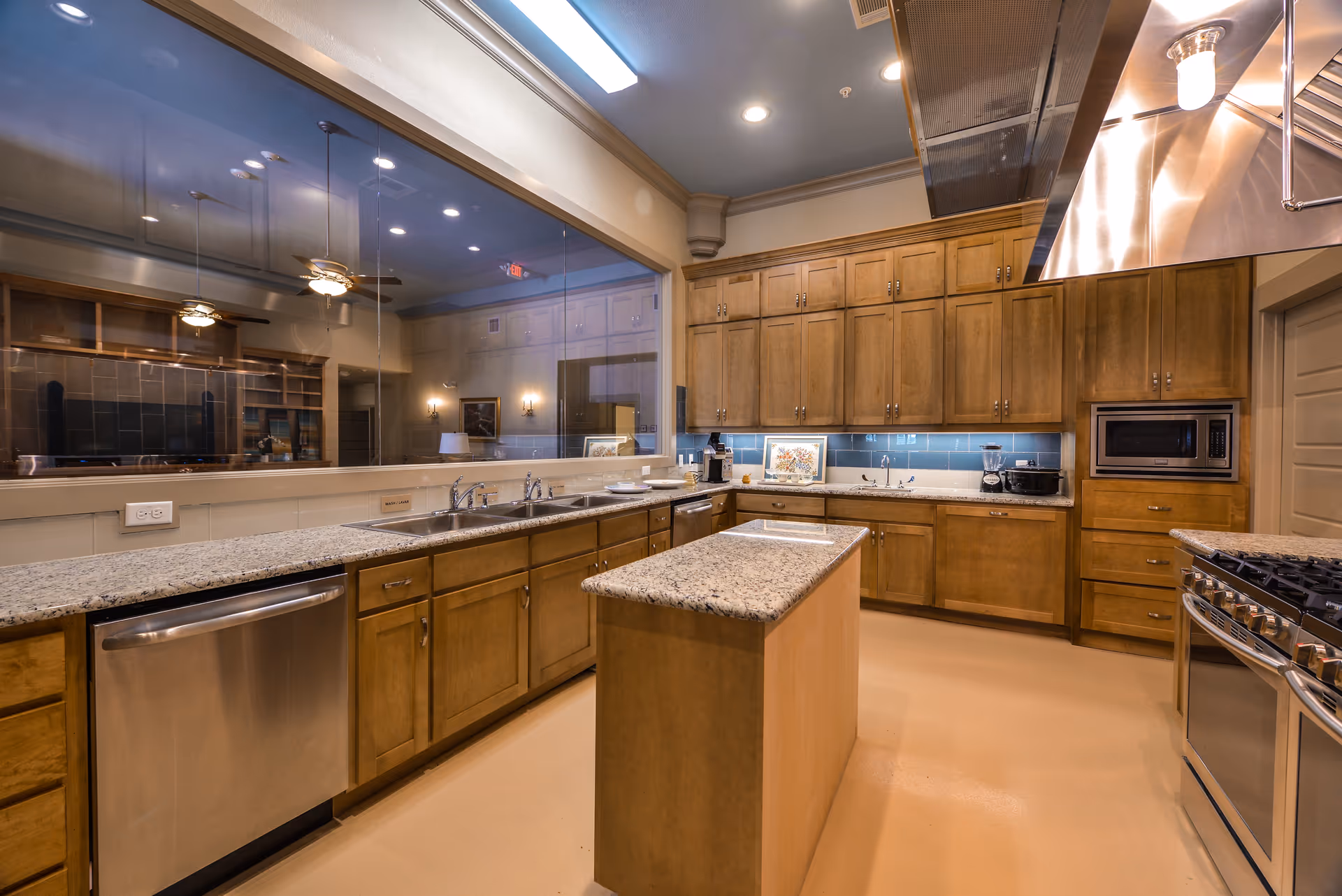 A modern communal kitchen with granite counters, wooden cabinets, an island, and stainless appliances.