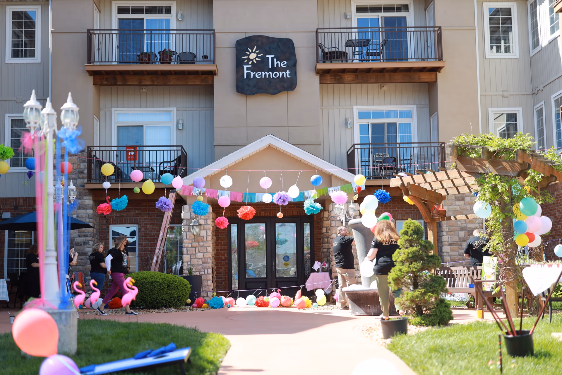 Front entrance of The Fremont senior living building decorated with colorful balloons, paper pom-poms and outdoor party decorations.