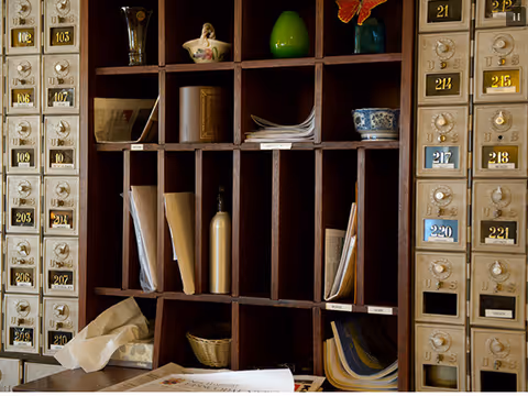 Wooden mail cubbies filled with letters and papers, flanked by two sets of vintage metal mailboxes with numbered brass plates.