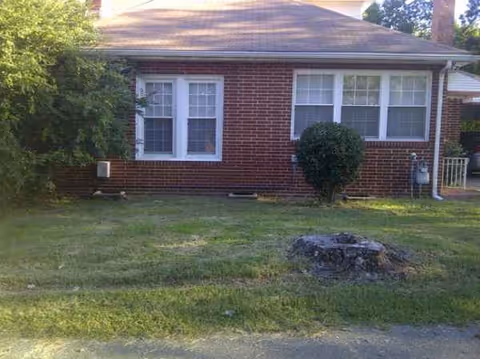 Brick single-story building with windows, a lawn, tree, and a stump in front.