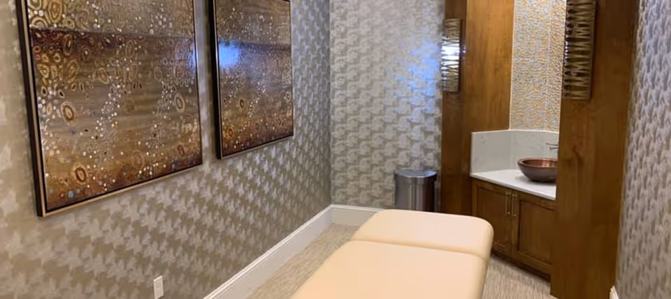 A small spa-style treatment room with a massage table, decorative wall art, and a sink with wooden cabinetry.