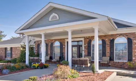 Brick senior living facility entrance with white columns and outdoor seating.