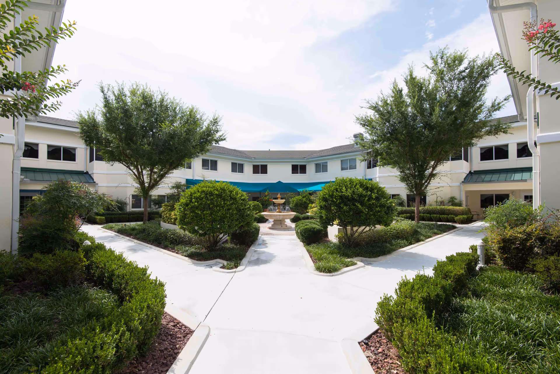 Symmetrical Majestic Oaks courtyard with trees, shrubs, walkways, and a central fountain.