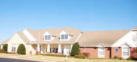 Single-story Brookdale Norman senior living building with brick exterior, manicured shrubs, and a blue sky.