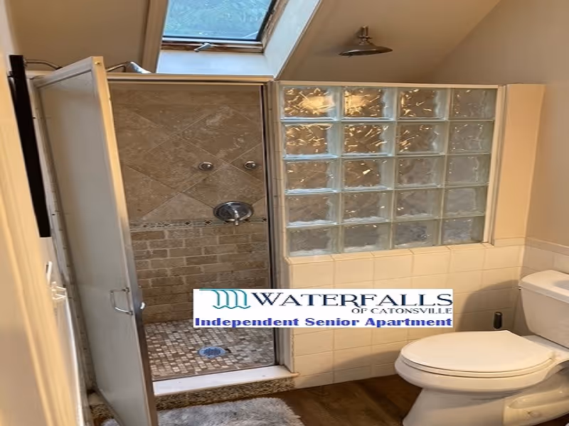 Bathroom with a walk-in shower featuring glass block walls and beige tiles, a white toilet, and a skylight above the shower area.