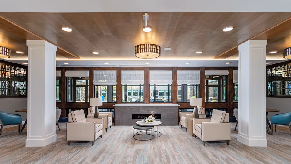 Spacious modern communal lounge with symmetrical armchairs, coffee tables, lamps, a central fireplace and large windows.