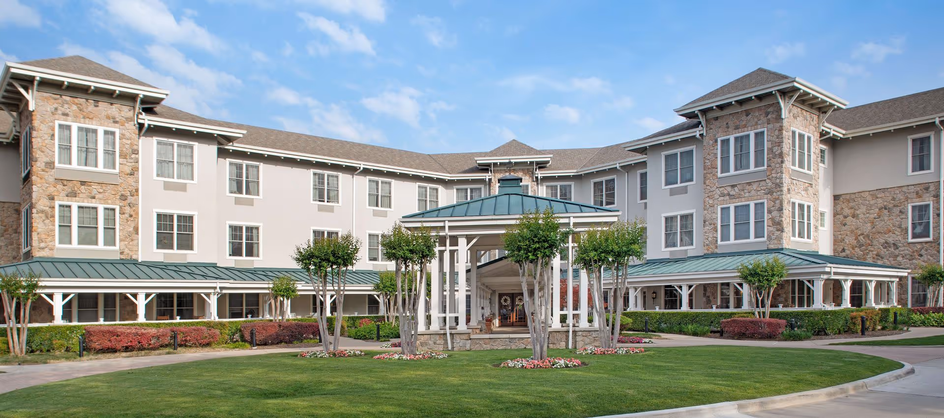 Front exterior of a multi-story senior living building with a covered circular entrance gazebo, manicured lawn, and landscaping.