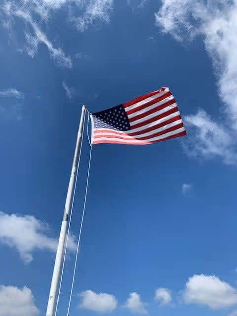 An American flag waving on a flagpole against a blue sky with scattered white clouds.