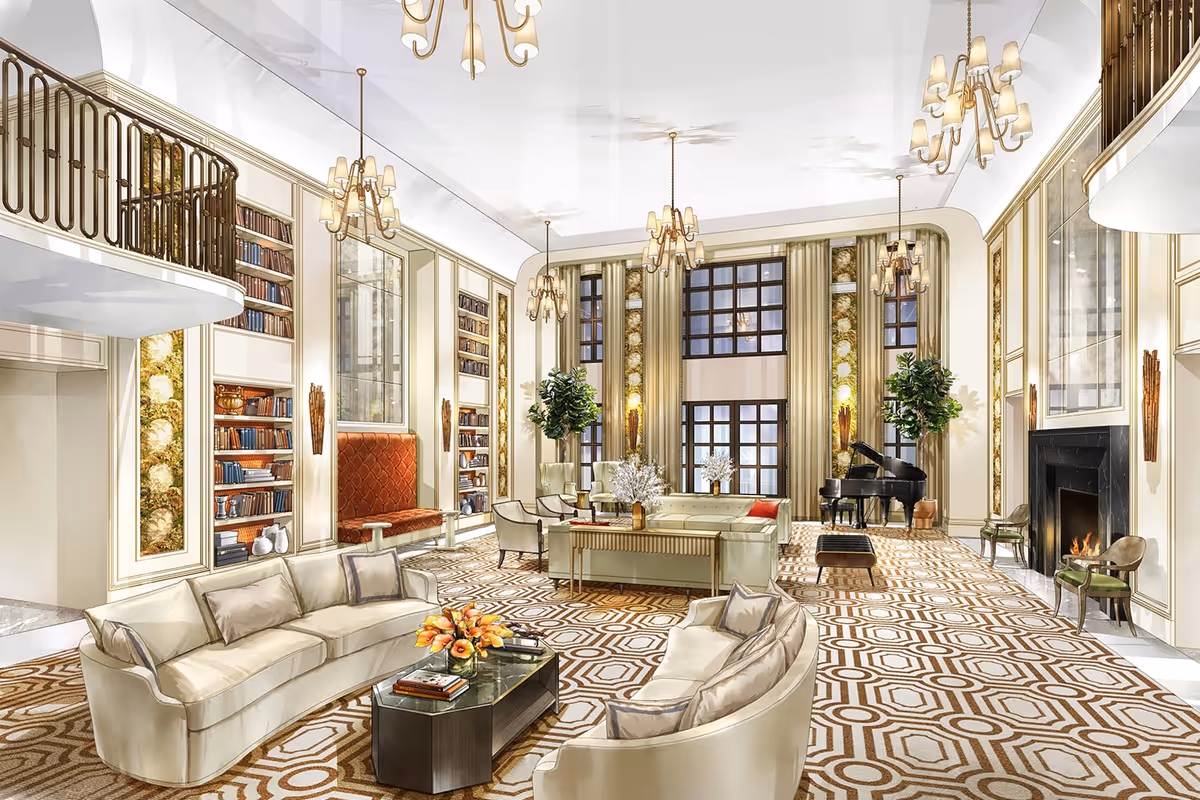 A spacious and elegant living room with high ceilings, large windows, and multiple chandeliers. The room features cream-colored sofas arranged around a central coffee table with flowers and books, a grand piano near the windows, built-in bookshelves, a fireplace, and decorative plants. The carpet has a geometric pattern, and the walls are adorned with gold accents and artwork.