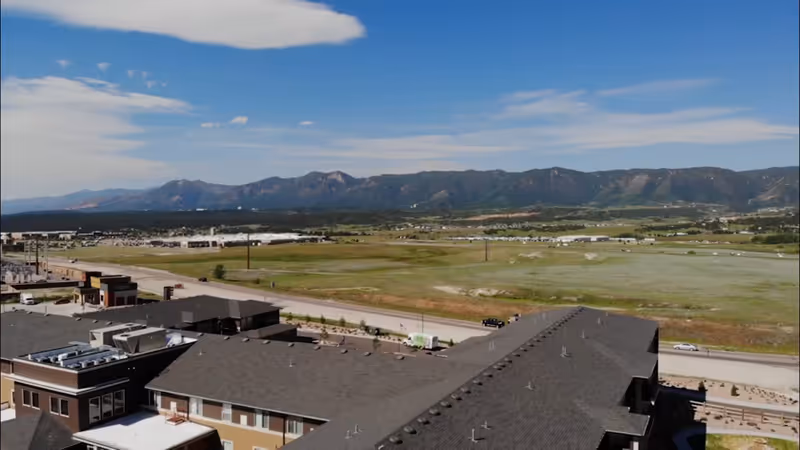 Aerial view of a senior living campus with building rooftops in the foreground, open fields, and distant mountains.