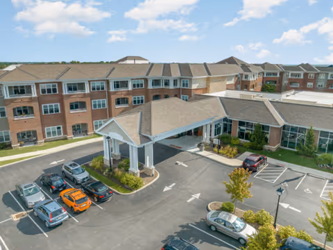 Aerial view of Twin Lakes Senior Living Community's three-story brick building with a covered porte-cochere and surrounding parking lot with cars.