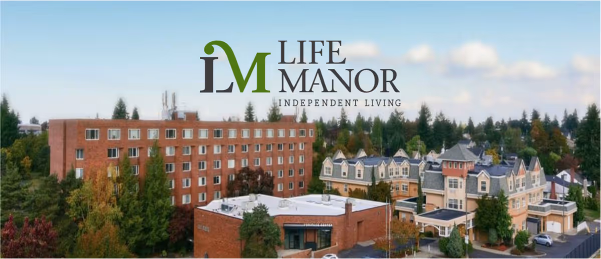 Aerial view of Life Manor Independent Living campus with a multi-story brick building and connected Victorian-style structures surrounded by trees.