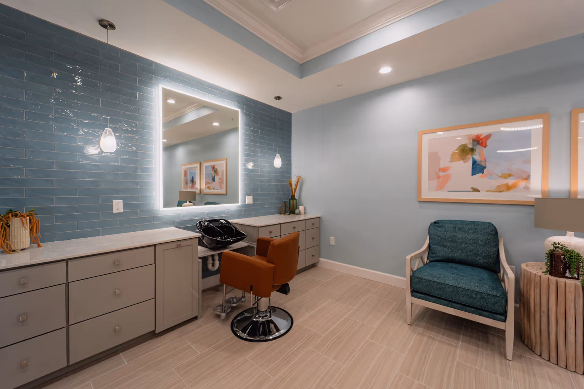 A well-lit salon-style interior with a styling chair, wash basin, backlit mirror, cabinetry, and a seating area.