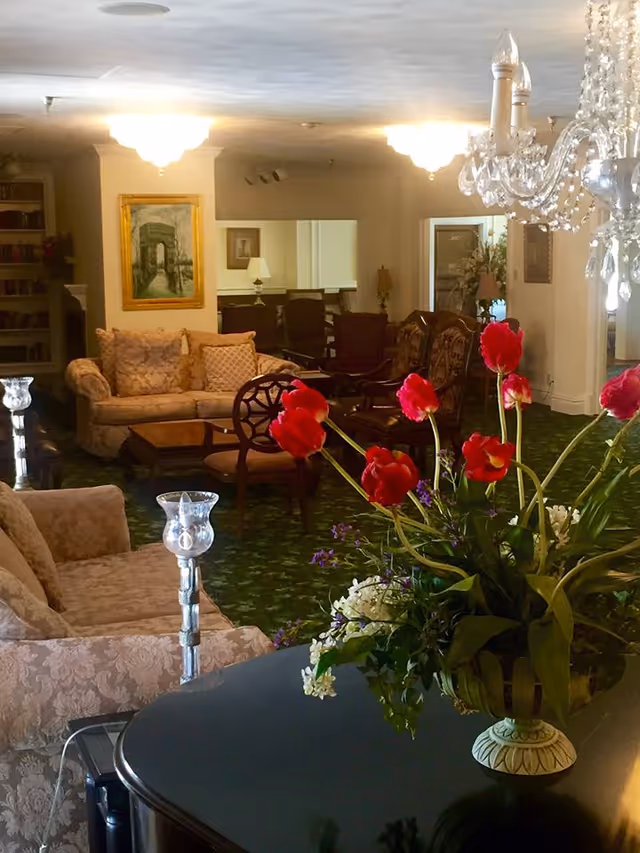 A decorated lounge with upholstered sofas and chairs, a chandelier, and a vase of red flowers in the foreground.