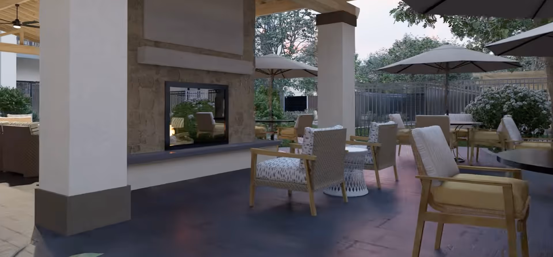 Covered outdoor patio with cushioned chairs, tables, umbrellas, and a double-sided fireplace.