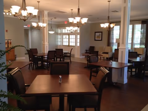 Spacious dining room with multiple wooden tables and chairs, chandeliers, and large windows.