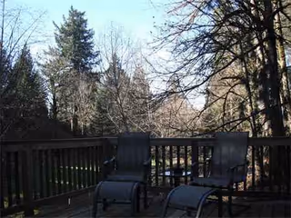 Wooden outdoor deck with lounge chairs and railing overlooking trees in the background.