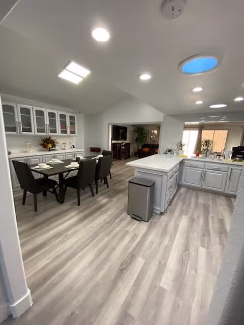 Open-plan bright kitchen and dining area with a white island, table and chairs, glass-front cabinets, and wood-look flooring.