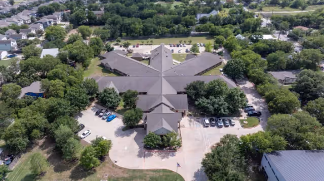 Aerial view of Riverside Nursing & Rehab campus with a multi-wing building, surrounding trees, and adjacent parking lots.