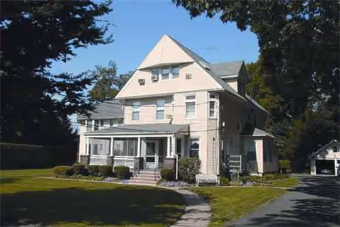 A two-story craftsman-style senior living home with a front porch and green lawn.