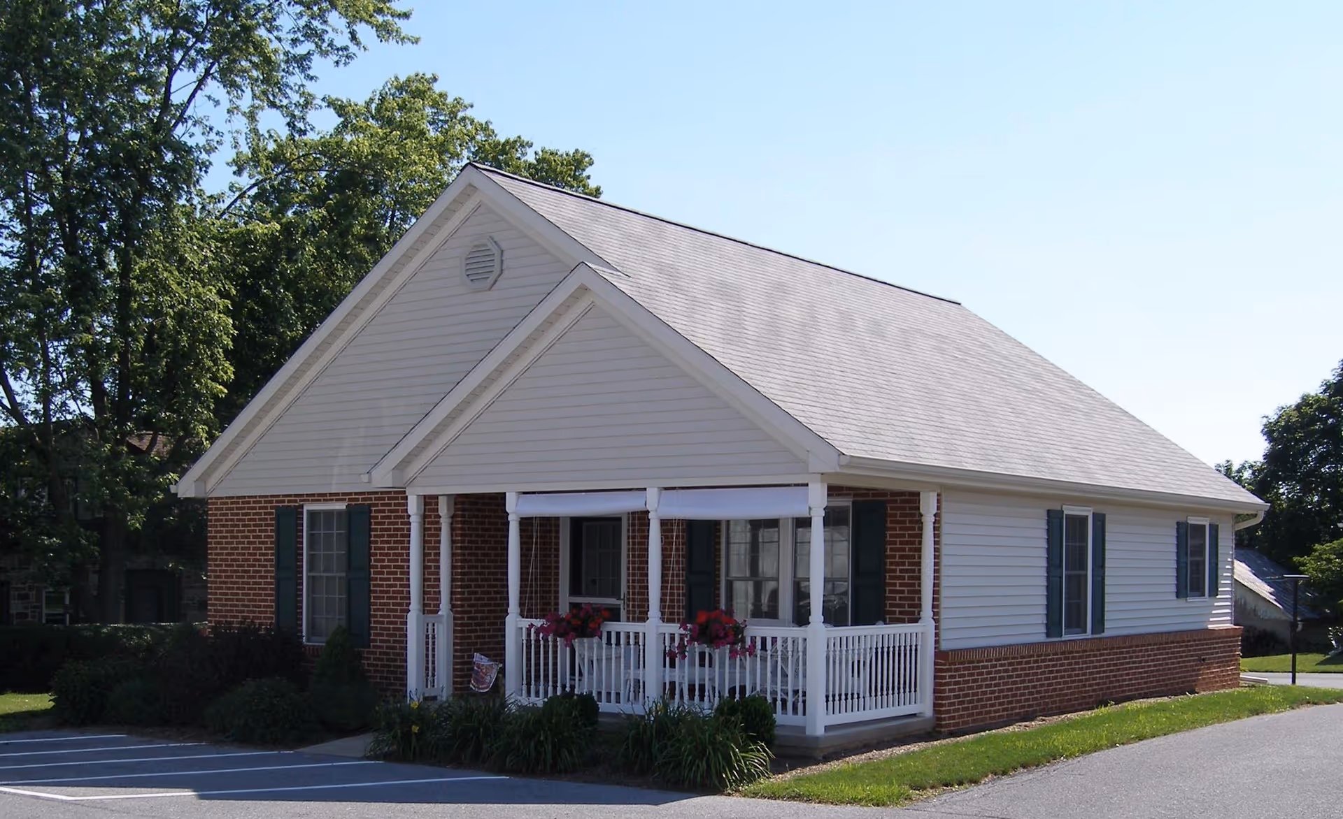 Small single-story brick and siding building with a covered front porch and white railing on a sunny day.