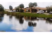 Single-story senior living facility along a pond, with palm trees and parked cars.