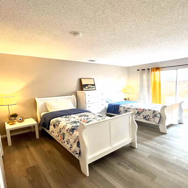 Two white twin beds in a bright bedroom with floral quilts and white furniture.