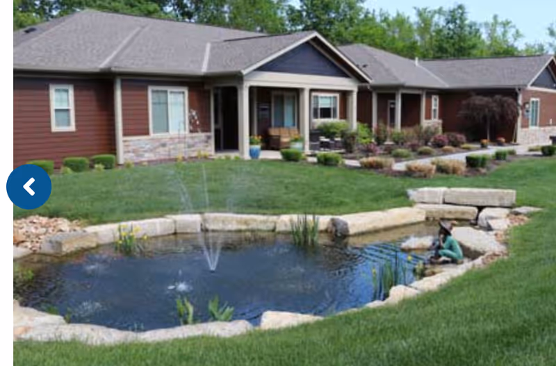 Single-story residential building with a landscaped lawn and a small stone-edged pond with a fountain.