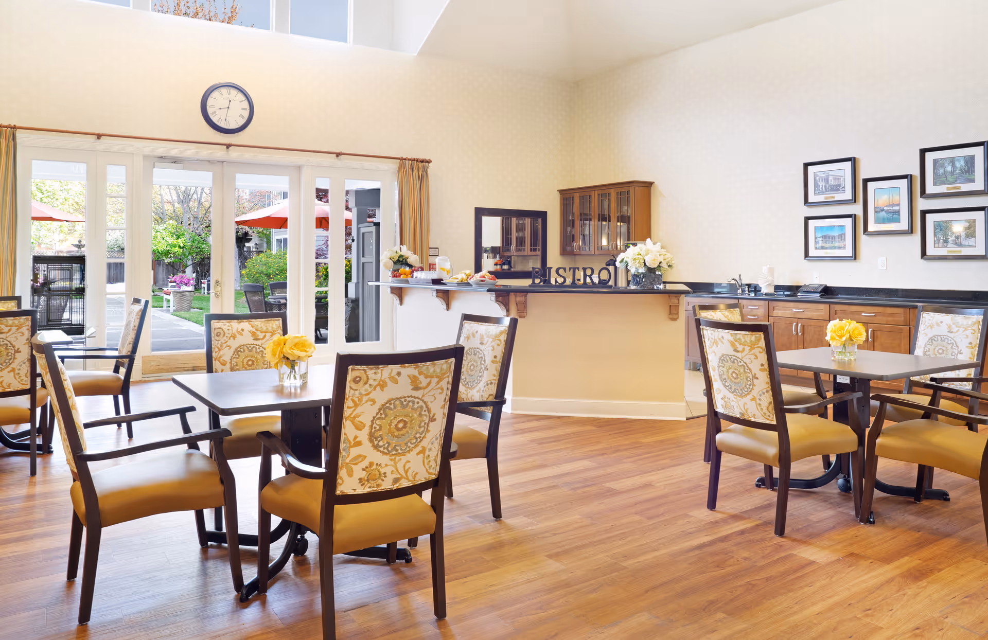 Bright dining room with wooden tables and upholstered chairs, a bistro counter, and glass doors opening to an outdoor patio.