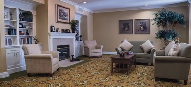 Communal living room with sofas and armchairs arranged around a coffee table and fireplace, built-in bookshelves, and a potted plant.