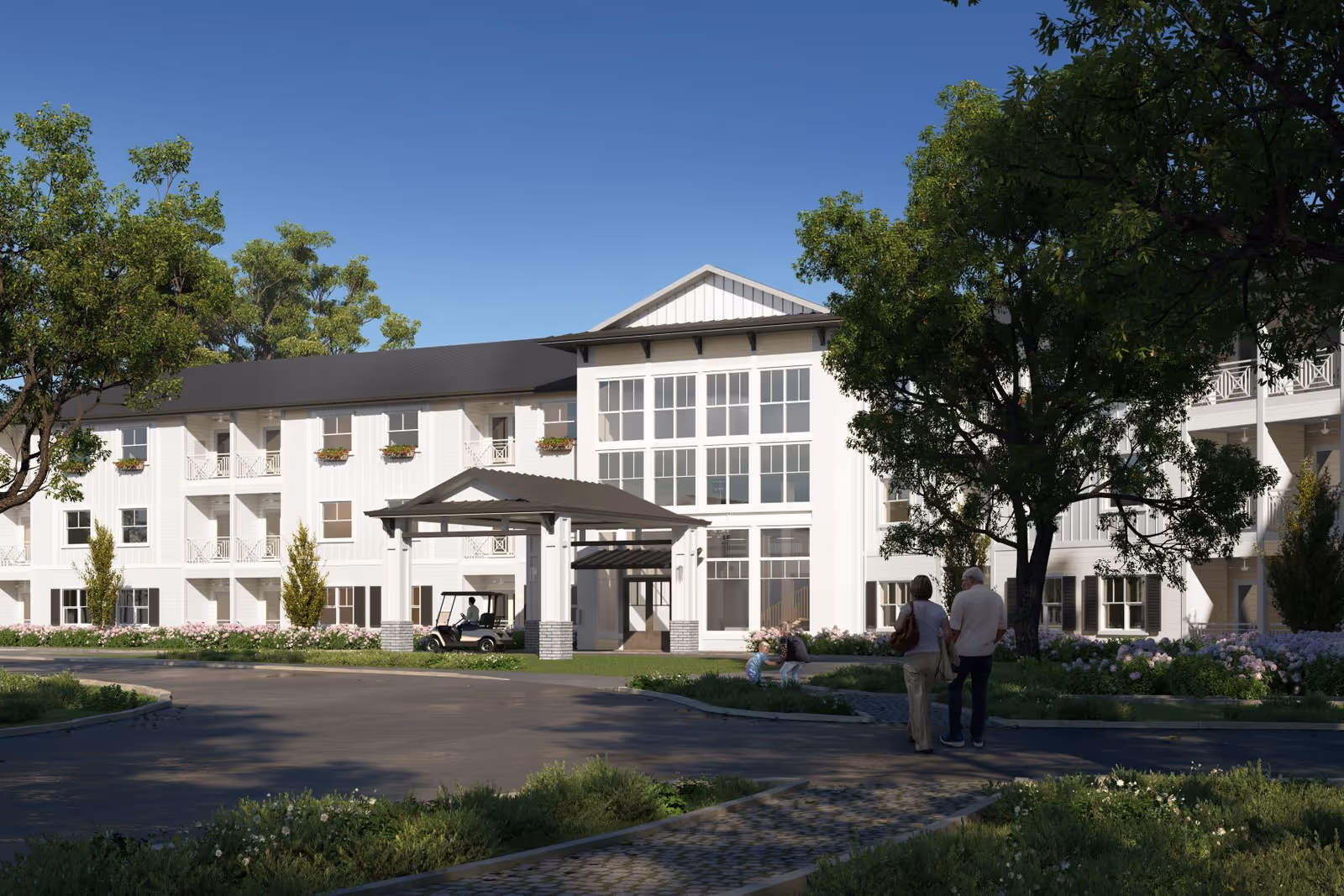 Front exterior of a three-story white senior living building with a covered entrance, landscaped grounds, and two people walking toward the entrance.