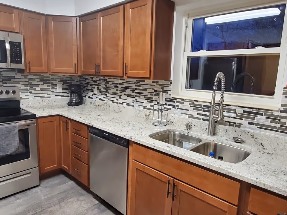 Kitchen with wooden cabinets, mosaic tile backsplash, granite countertops, stainless steel sink, dishwasher, and oven.