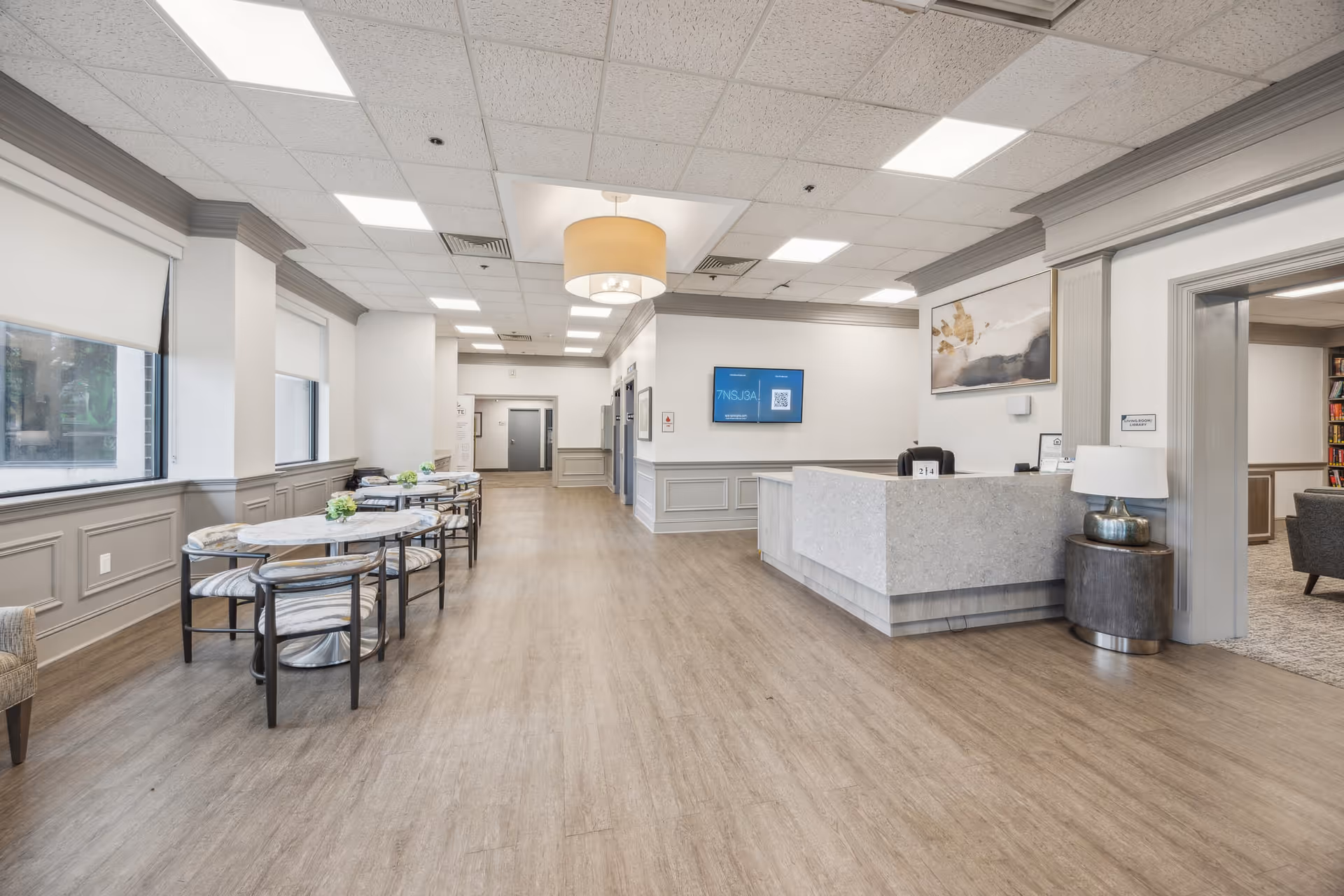 Bright reception lobby with a check-in desk, seating tables, and large windows.