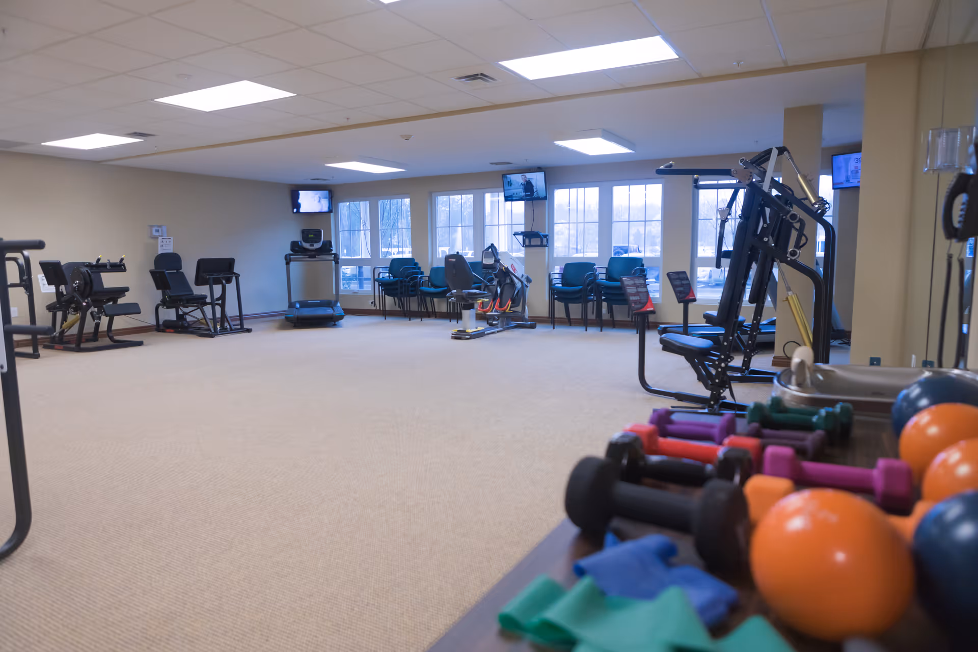 Bright fitness/therapy room with exercise machines, dumbbells and stability balls in a senior living facility.