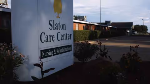 Exterior view of Slaton Care Center sign beside the building and landscaping.
