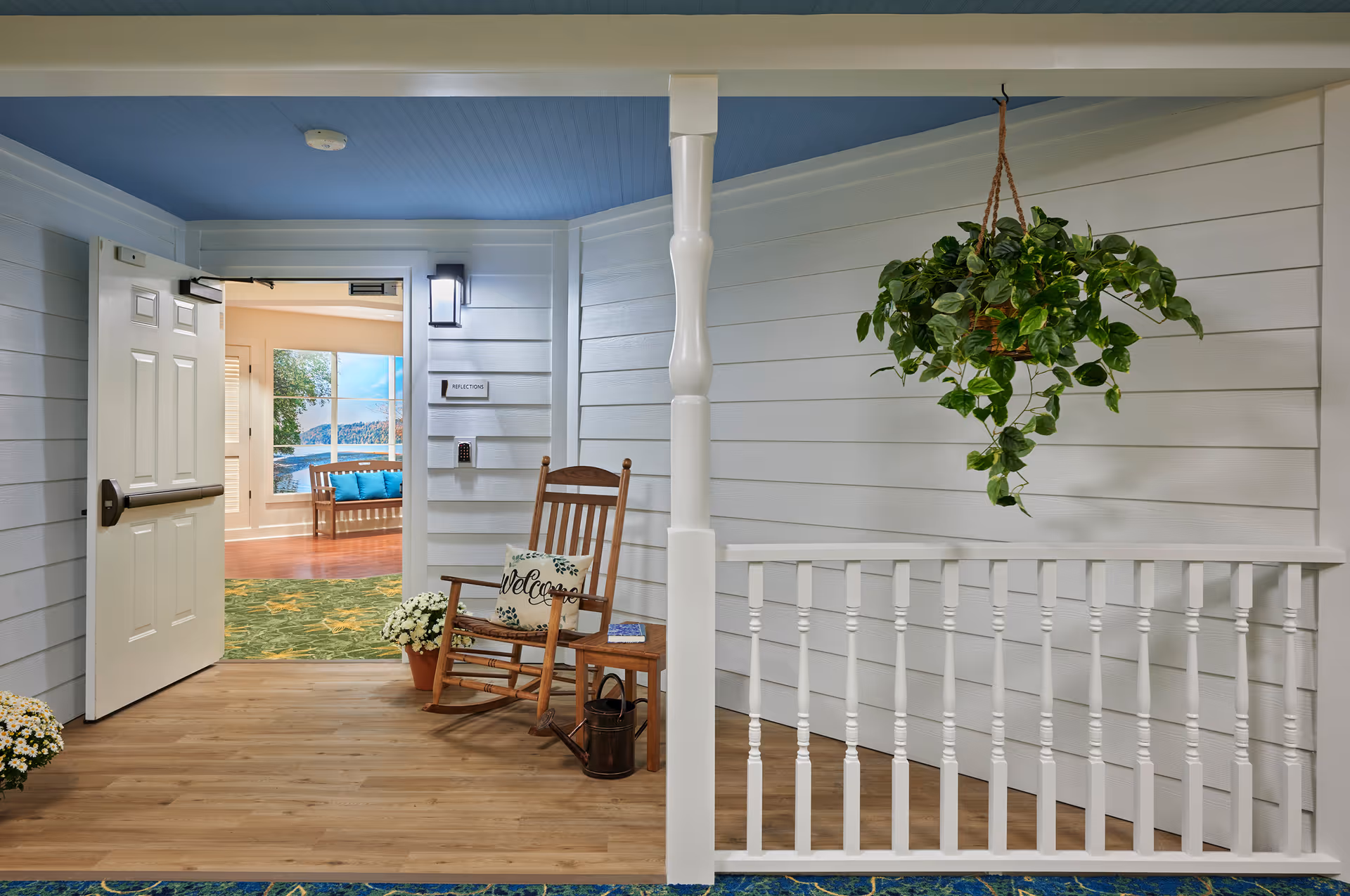 Porch-style interior area with a wooden rocking chair, potted plants, a hanging plant, and an open door leading to a lounge.