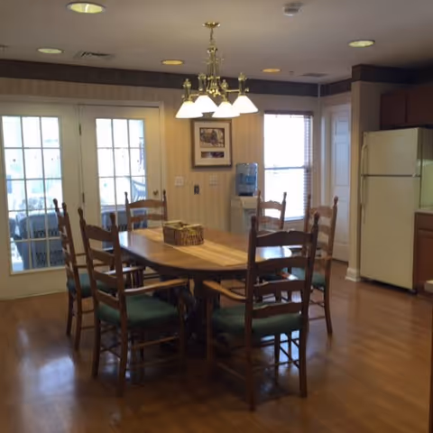 Dining area with a wooden table and six chairs under a chandelier, hardwood floors, a refrigerator, and French doors.
