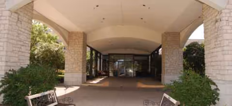 Covered entrance to a senior living facility with stone pillars and benches.