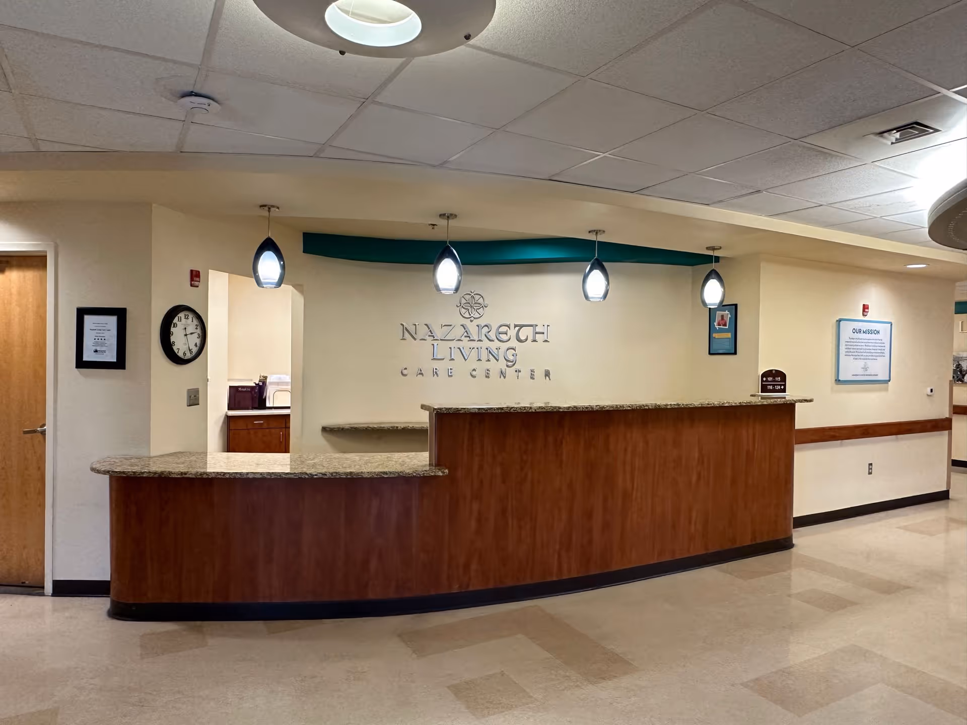 Reception desk and lobby of Nazareth Living Care Center with pendant lights and wall signage.