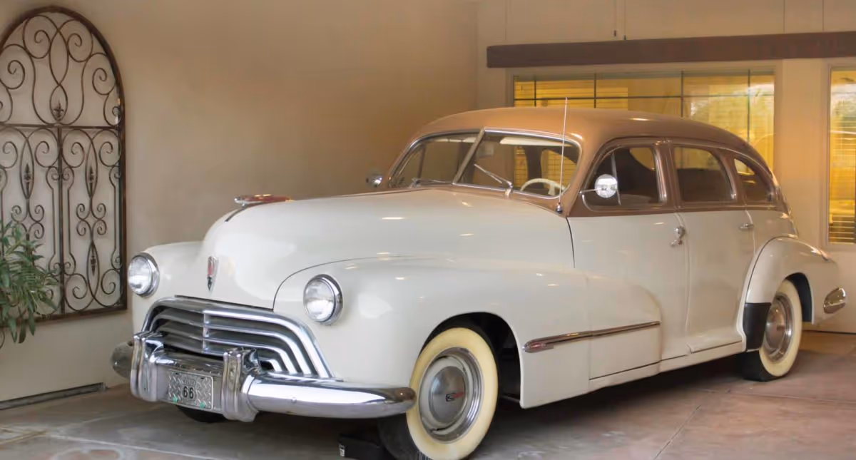 A cream-and-brown vintage car parked indoors in a showroom-like room with decorative wall art and windows.