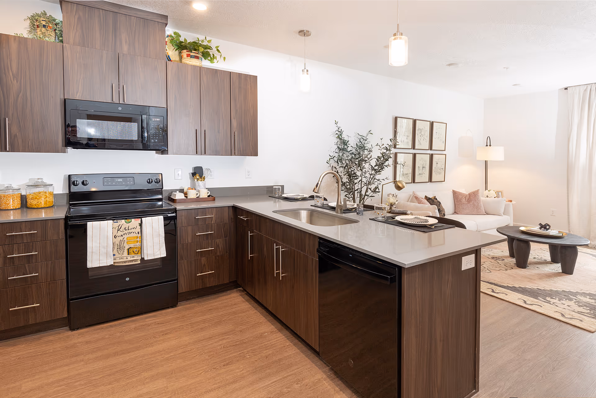 Modern open-plan kitchen with dark wood cabinets and an island with sink, looking into a furnished living area.