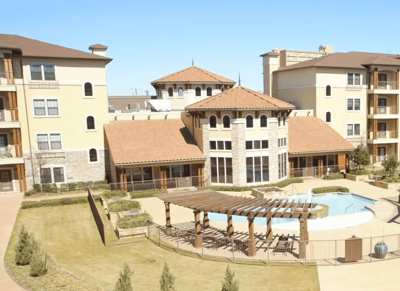 Courtyard and pool area of a Mediterranean-style senior living complex with multi-story buildings and a wooden pergola.
