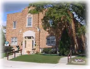 Front exterior view of a brick senior living facility entrance with trees and walkway