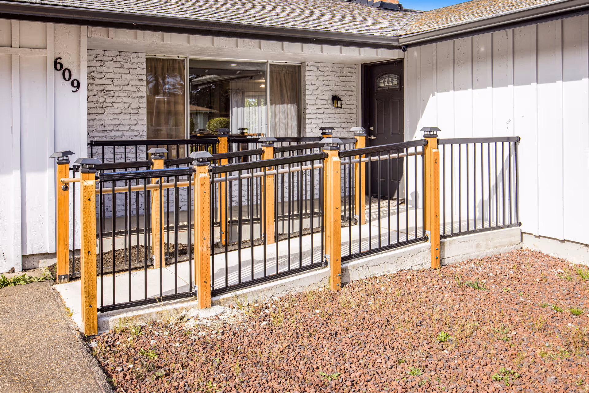 Front entrance of a single-story building with a concrete wheelchair ramp and black metal railings, house number 609 on white siding.