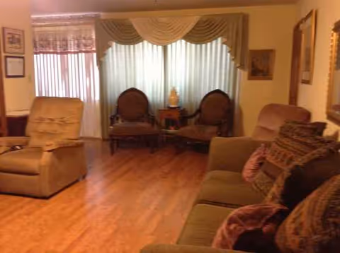 Cozy senior living room with sofa, recliner, ornate chairs, and draped windows.
