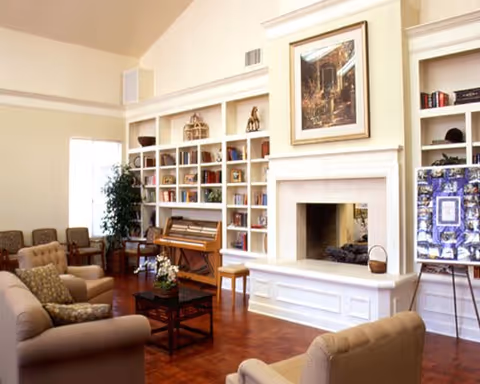 Spacious common living room with sofas and armchairs, built-in bookshelves, a fireplace, and a piano.