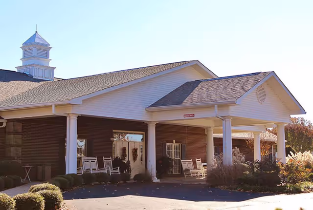 Front entrance of Sugar Creek Senior Living with white pillars and rocking chairs on covered porch.