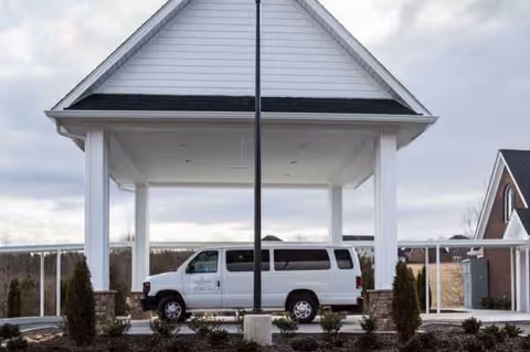 A white van parked under a covered entrance at a senior living facility exterior.
