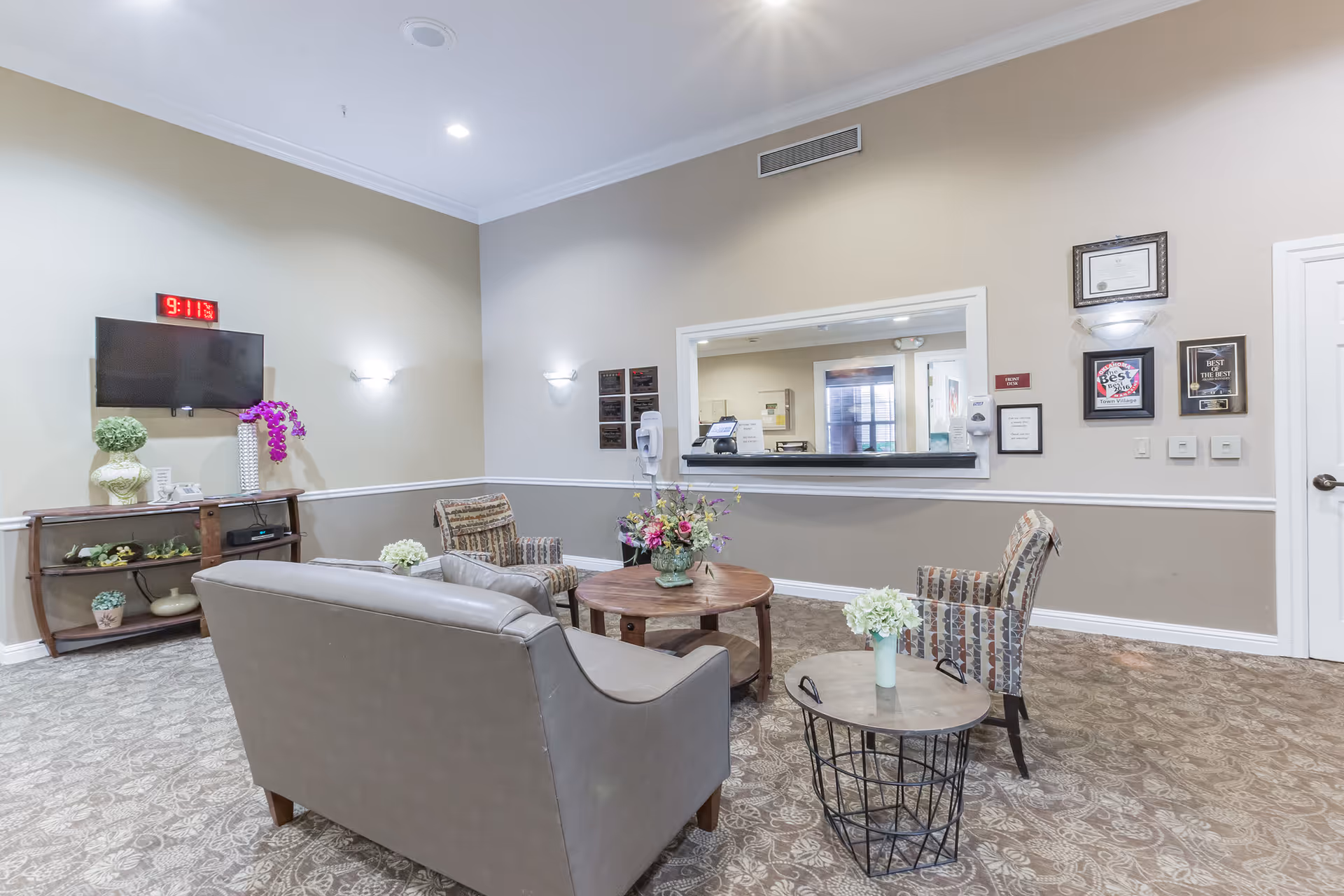 Reception lounge with sofas and chairs around coffee tables facing a TV and a service window.