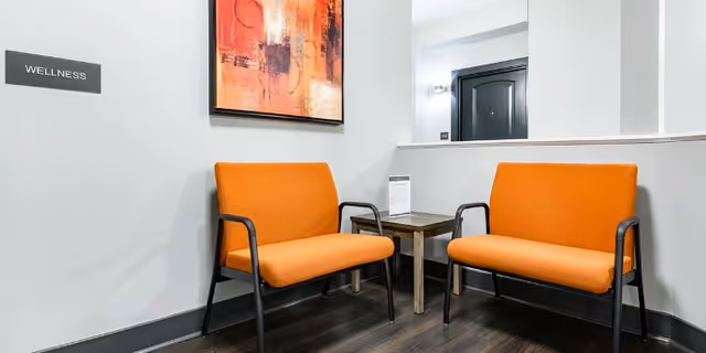 Two orange chairs with a small table in a wellness waiting area.